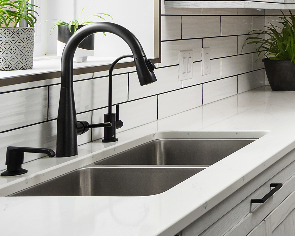 Kindred® stainless steel kitchen sink. Sink is shown with black faucet, and is undermounted on a white countertop. Photo by Illia Sternichuk.