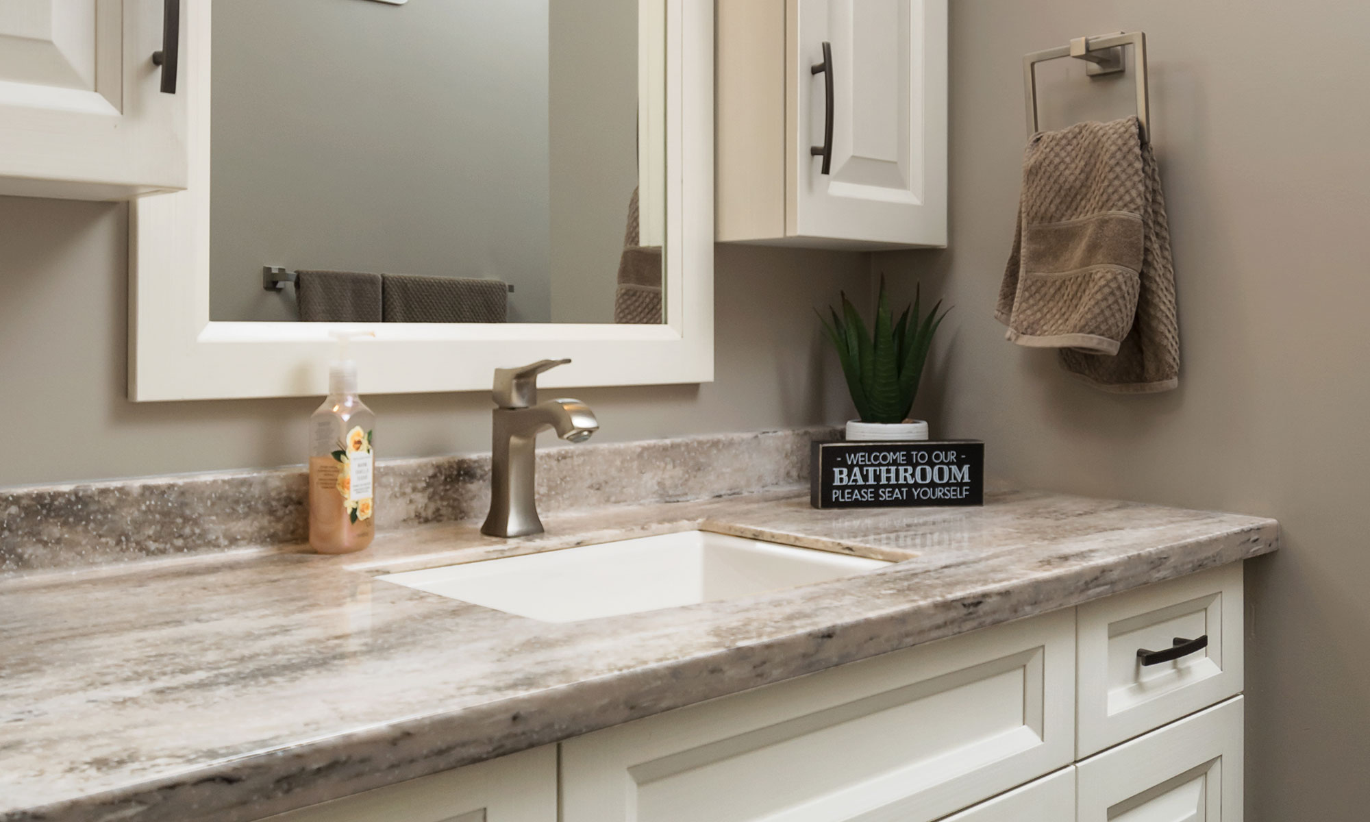 Solid surface vanity countertop with a black/gray/beige natural pattern, installed on a white recessed panel vanity with matte black cabinet pulls. Photo by Illia Sternichuk.