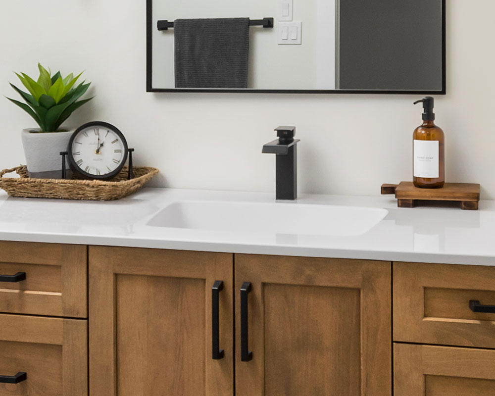 shorrock-cultured-marble-countertop-1000x800 White cultured marble vanity countertop and integrated sink with matte black waterfall faucet. The countertop is installed on a light brown flat-panel vanity with black cabinet pulls. A large mirror is framed by single-light sconce lamps with clear glass globes off to each side. Photo by Illia Sternichuk.