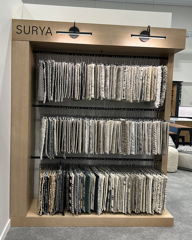 A display featuring three separate tiers of Surya area rug samples at the Creative Kitchens showroom.
