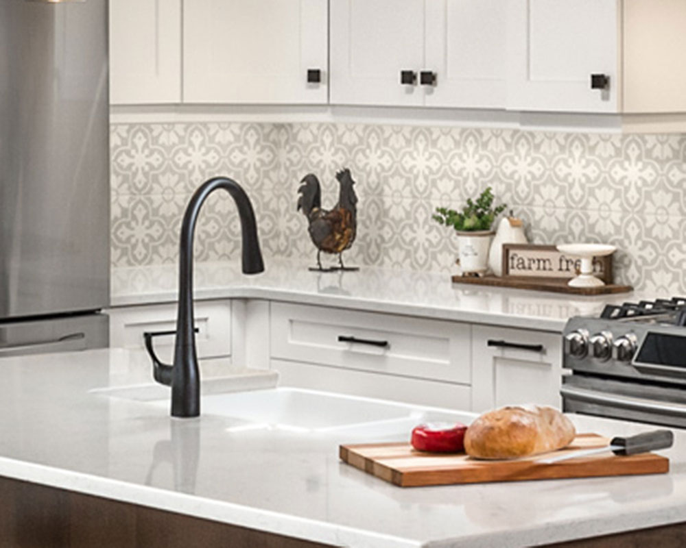 Kitchen island with an undermount sink and Kohler faucet. The faucet is matte black with a single lever. A cutting board with break and cheese sits on the countertop.